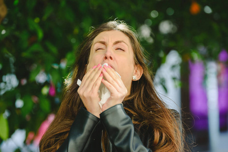 在有鼻窦问题的花园里，由于春季对花粉过敏而吹鼻子的年轻女子