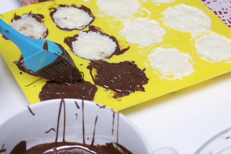 一个女人涂巧克力填充椰子和炼乳。 甜点的配料在桌子上。 用椰子和炼乳烹饪糖果。 在白色和黑色巧克力的釉里。
