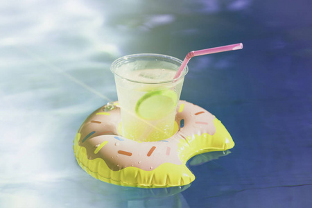 在游泳池里, 在充气甜甜圈玩具上, 品尝冰和新鲜的柠檬汁的美味鸡尾酒。夏季在游泳池度假和放松时间。阳光效应与波纹水反射