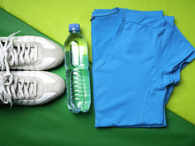 平躺在绿色运动垫背景上运动T恤裤子白色运动鞋健身项目顶部视图