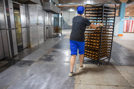 面包店工人把饼干放在大型工业烤箱,面包和糖果食品厂内部照片