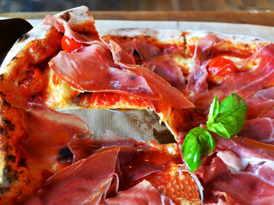 意大利比萨饼与培根番茄草药在一张木桌上，用铲子供应。 快关门。 披萨餐厅的概念。 宏观披萨