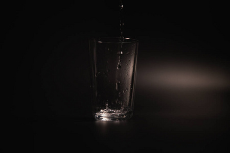 水倒在黑暗背景上的透明玻璃中