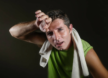 年轻的疲惫和疲惫的运动男人用毛巾擦干汗水，经过艰苦的锻炼和健身训练，在健康的生活方式概念中孤立于黑暗的背景中，所有的汗水和呼吸都