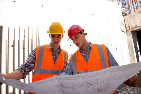 施工经理和工程师穿着工作服和安全帽, 在建筑工地上探索项目文件