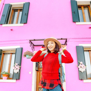 年轻快乐的旅行者女人在布拉诺岛威尼斯五颜六色的房子里摆姿势。 意大利旅游概念