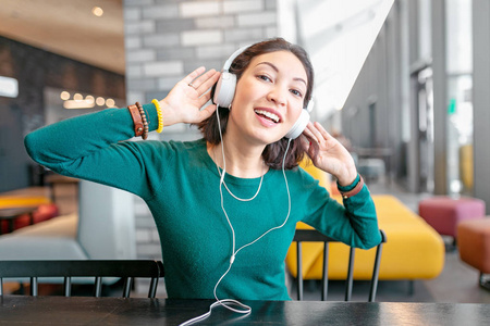 快乐的亚洲女人用耳机欣赏音乐，在酒店大厅或咖啡馆放松