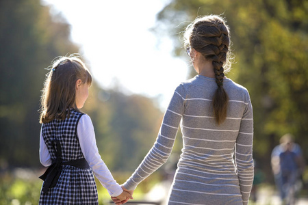 在阳光明媚的户外温暖的日子里,女孩和母亲穿着连衣裙,手牵手.照片