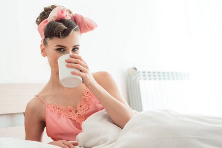 美丽的女人喝着她的早晨咖啡还在床上