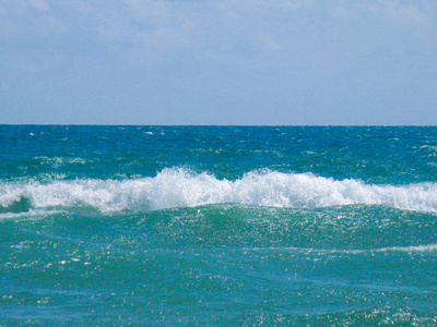 海咸的纯蓝色波浪在当地海滩的沙滩上翻滚。 晴天的低浪。