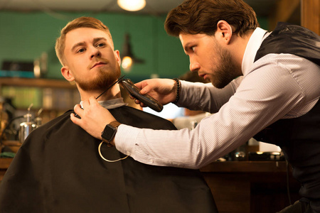 年轻人剃胡须，由理发店服务的专业理发师修剪，客户消费主义，奢侈，福利，舒适，理发专业，嘻哈。