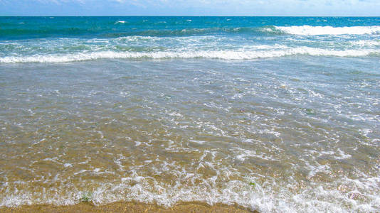 海咸的纯蓝色波浪在当地海滩的沙滩上翻滚。 晴天的低浪。