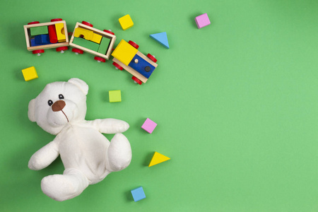 儿童玩具背景。白色泰迪熊, 木制玩具和绿色背景上的五颜六色的方块。顶视图, 平面布局