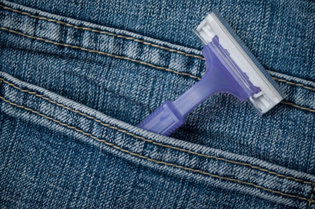 蓝色牛仔裤口袋里的紫色一次性塑料剃须刀特写