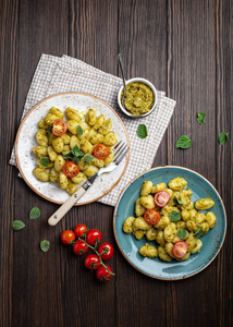 在带有绿色Pesto酱西红柿和草本植物的盘子中的Gnocchi，在乡村的木制背景下，靠近顶部的视野。 意大利菜的传统菜肴