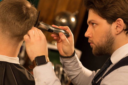 裁剪的特写镜头，一个英俊的年轻专业理发师，看着集中给他的客户理发，使用剪刀修剪设备，师，理发店。