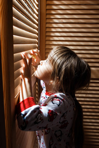 穿着睡衣的小女孩躲在壁橱里, 拿着木门