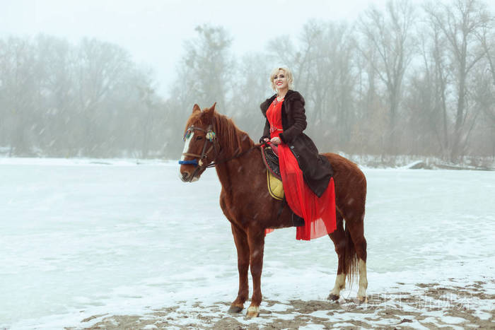 穿着红色裙子坐在马上的女人他们站在一个结冰的湖旁那里正在下雪