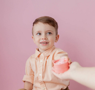 快乐的小男孩与礼物。照片隔离在粉红色的背景。微笑的男孩拿着现在的盒子。节日和生日的概念