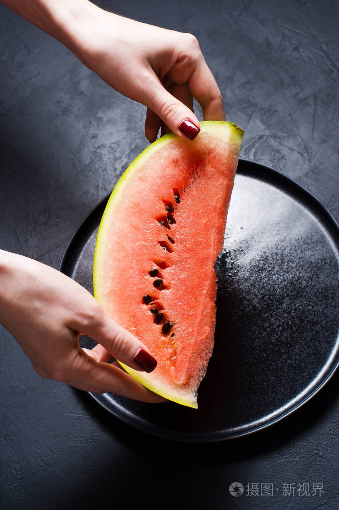 手拿着一片西瓜. 深色背景顶部视图