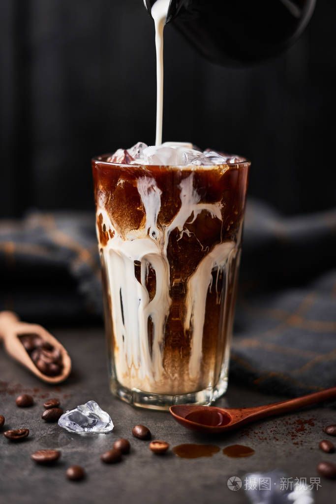 冰咖啡放在一个高杯子里,上面倒着奶油,咖啡豆放在黑色的木制背景下的