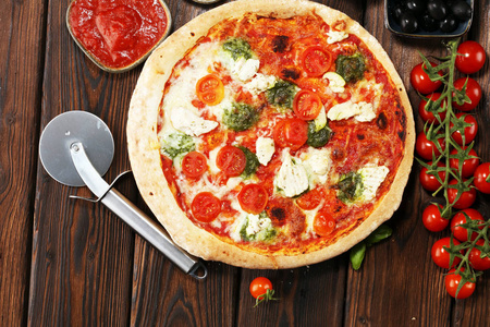 带西红柿的披萨，莫扎雷拉奶酪，黑色橄榄和罗勒。 木制比萨饼板上美味的意大利披萨。 意大利披萨