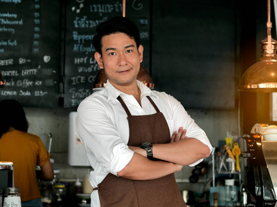 快乐的亚洲咖啡师在酒吧前交叉手臂，生活方式的概念。