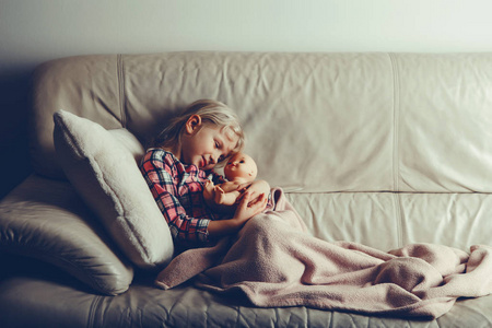 孩子玩玩具。可爱的高加索女孩抱着婴儿娃娃。孩子晚上躺在床上，晚上躺在室内。与电影过滤器风格。快乐的童年生活方式。