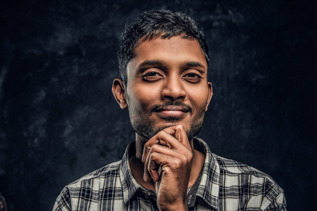 一个英俊的印度小伙子穿着格子衬衫, 手放在下巴上, 看着带着沉思的相机的肖像