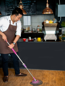 咖啡厅亚洲咖啡师清洁地板。