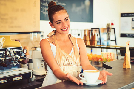 今天的好心情是由咖啡赞助的。咖啡店里的女咖啡师巴里斯塔微笑着供应一杯热饮饮料。漂亮的女人站在咖啡馆柜台后面。在咖啡屋煮咖啡