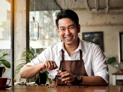 快乐的亚洲咖啡师男人在桌子上磨咖啡豆的生活理念。