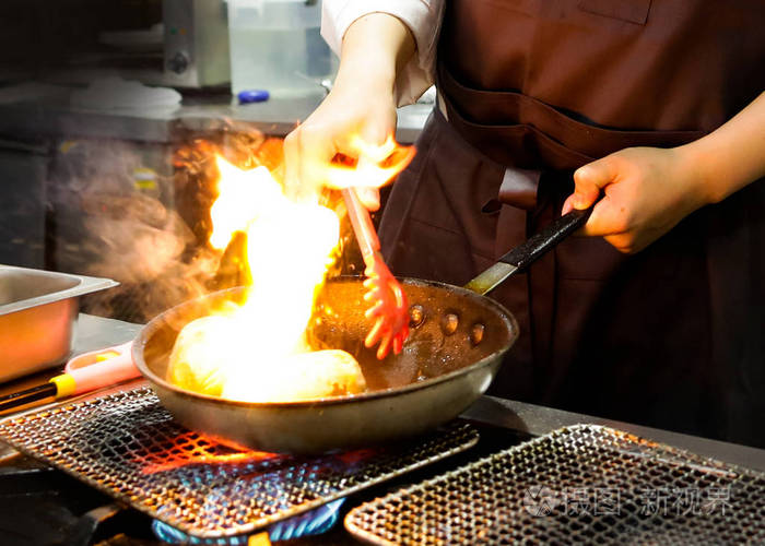厨师在厨房灶台上用火煎锅烹煮厨师在餐厅灶台上用锅烹煮