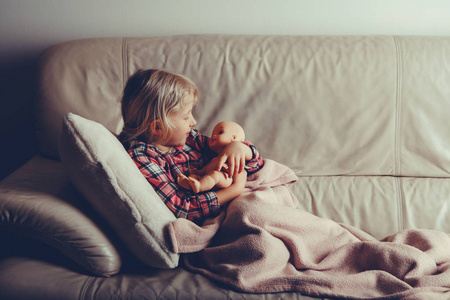 孩子玩玩具。 可爱的高加索女孩抱着娃娃。 孩子晚上躺在床上，晚上晚上躺在室内。 与胶片过滤器风格色调。 快乐的童年生活方式。