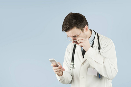 年轻可爱的医生学生，手里拿着智能手机，在一个蓝色的孤立的背景下和朋友交谈。电气冲突概念和连接