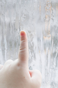 s hand draws patterns on the frozen window in winter