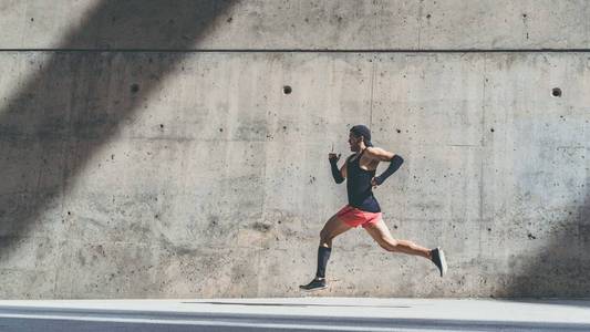 肌肉发达的男运动员短跑运动员跑得很快, 在户外锻炼, 在灰色混凝土背景下慢跑, 并有文字或广告内容的复制空间区域。侧视图, 全长