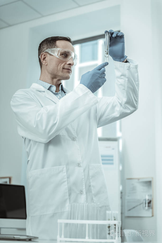 穿着白色长袍和携带样品的橡胶手套的细心科学家
