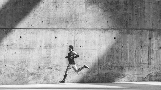 肌肉男子运动员短跑跑快, 在户外锻炼, 在灰色混凝土背景下慢跑, 有文字或广告内容的复制空间区域。宽, 全长。黑色白色
