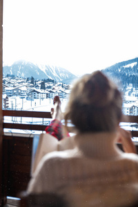 瑞士冬季山脉的宁静。 女人喝着热腾腾的美式咖啡，读着一本有趣的书。 把她的腿放在扶手上，戴着睡衣。 舒适的家庭氛围。