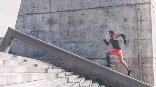 肌肉发达的西班牙深色皮肤的男运动员建立了运行在楼梯上的速度。为短信或广告内容提供带有复制空间区域的背景墙