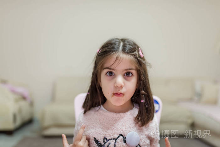 小可爱的女孩一边看着摄影师一边吃着带着滑稽表情的惊喜巧克力