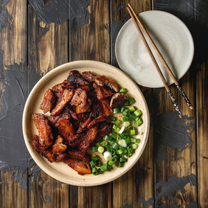 中国传统菜广东烧烤猪肉肚与葱在陶瓷盘子与筷子在深色木板背景.