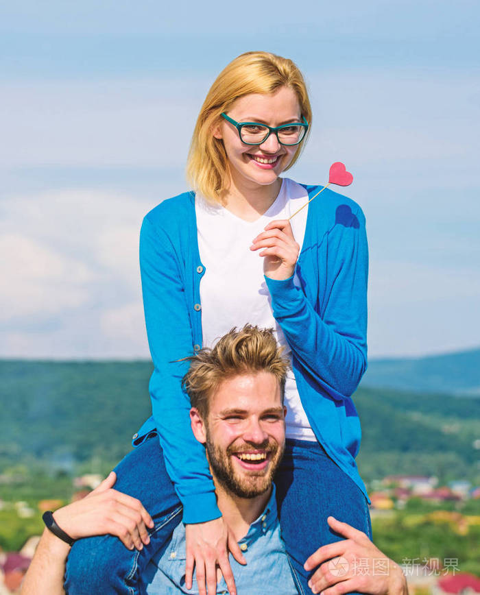 男人扛着女朋友的肩膀天空的背景浪漫的日期概念女人握着爱的象征的心