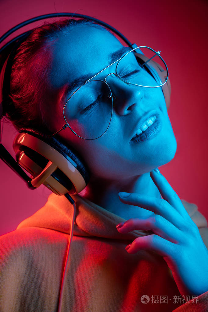 时尚漂亮的女人与耳机听音乐在霓虹灯背景