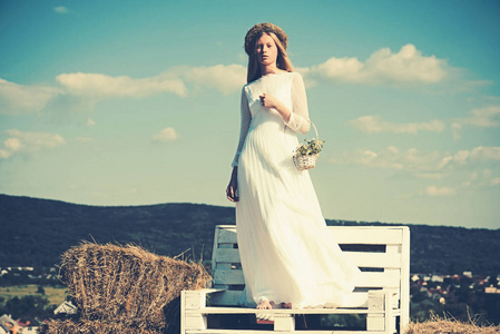 白化女孩与花, 自然秀丽。女新娘在婚纱礼服上的木凳上。的女人在花环上长的金发。在阳光明媚的蓝天上度假的时装模特