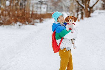 在冬季公园里, 穿着温暖时尚的衣服, 穿着背包摆姿势的时髦年轻女子的肖像。友谊宠物和人类