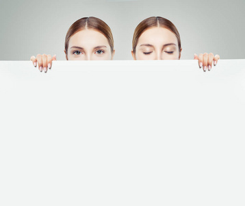 两位年轻女性上下打量，展示白色空纸卡背景，并提供广告营销或产品放置的复制空间