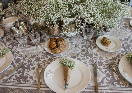 婚礼装饰的桌子花束，白色的花，在玻璃罐和艺术纸盘上的第一个计划，陀螺仪饼干在盘子上