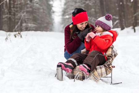 母亲和孩子女孩在下雪的冬天在大自然中散步，玩得开心，喝茶。 冬季概念。